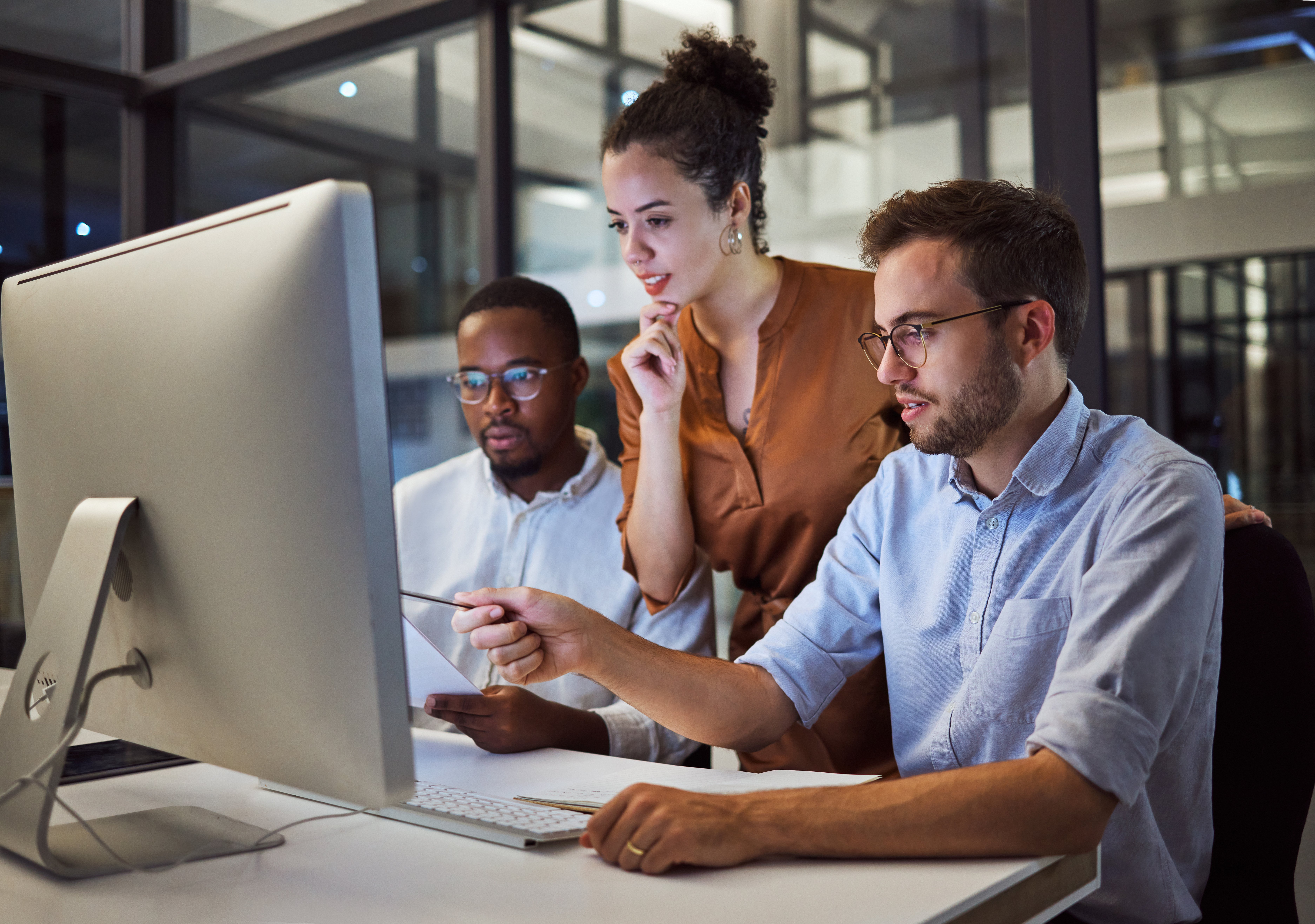 Three professionals look at a computer screen together. 